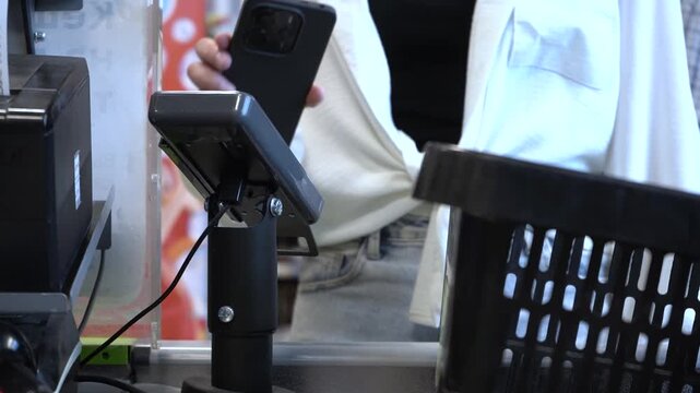 Checkout Process: A Close-Up View of Mobile Payment at the Register with a Customer's Hand Approaching a Scanner in a Retail Environment