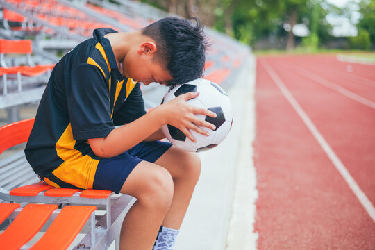 Sad and depressed Asian youth athlete sitting lonely on a stadium bench facing emotional stress and anxiety. Concept of youth sports competitive pressure, parental expectation failure, child mental he