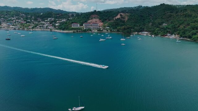 Aerial drone shot of a speedboat cruising through the turquoise waters of Samana Bay, passing islands and coastal resorts, leaving a distinct white wake behind