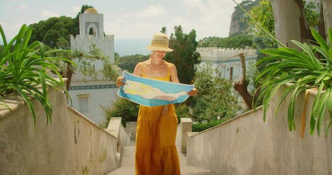 Woman exploring Capri hillside, checking map near white villa and distant sea view