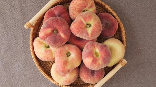 Fresh ripe flat peaches rotating in a wicker basket