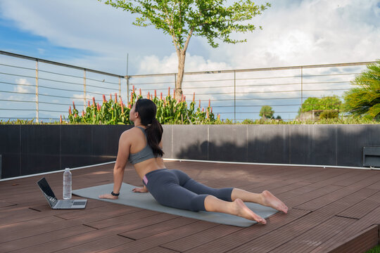 Woman practicing yoga outdoors cobra pose with laptop