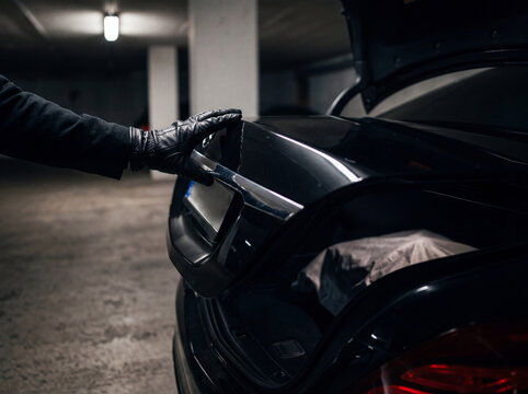 Person wearing black gloves closing the trunk of a black car in an underground parking garage with leather gloves transportation