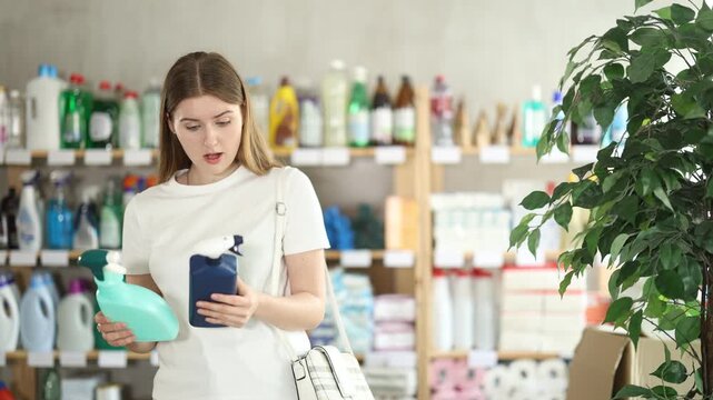 Young woman in summer clothes holds two sprays with sprayers to clean tiles and surfaces in the kitchen. Shopper choosing cleaning sprays in supermarket. High quality 4k footage