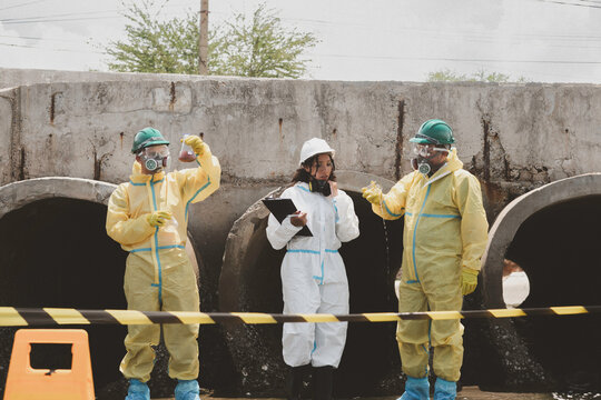 Scientists in chemical protective suits are at a water passage, collecting water samples and analyzing data on laptops to monitor pollution and contamination in the industrial area.