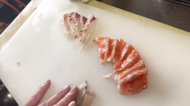 Japanese chef slicing fresh olive flounder for sashimi with sliced salmon on a cutting board, overhead view in an izakaya kitchen