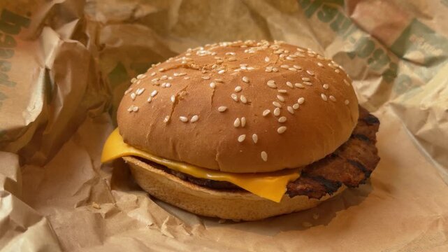 Grilled cheeseburger with sesame bun resting on crumpled fast food wrapper indoors