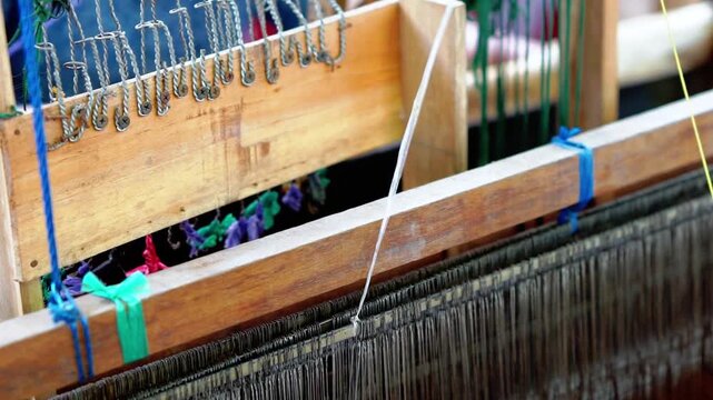 A textile artisan is weaving a piece of fabric, a traditional Indonesian textile.