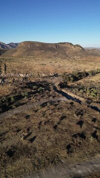 Aerial vertical view of a rural road and a small pond in a wide highland valley framed by mountains in Aguascalientes, Mexico.