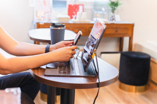 Side angle view of woman using a smartphone while working on a tablet in cafe.