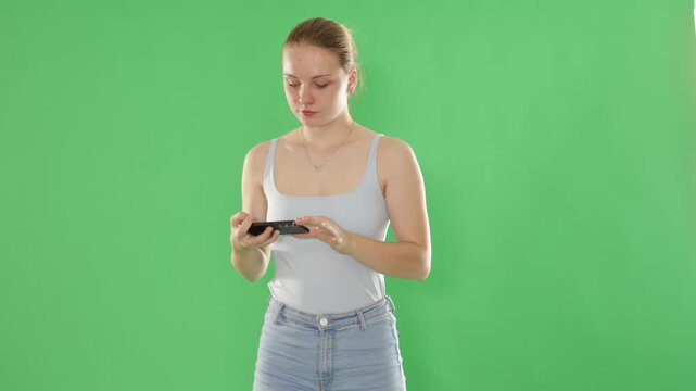 Teenage girl in blue top takes selfie on a smartphone on a green background. Chroma key compositing. High quality 4k footage