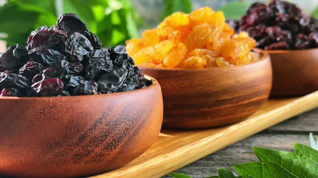 Three raisin varieties in wooden bowls with slow rightward camera movement and shifting focus on a rustic tabletop