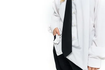 Close up of a teenage girl standing casually with one hand in a pocket while wearing an oversized white shirt and black necktie on a white studio background with copy space. © o_lypa