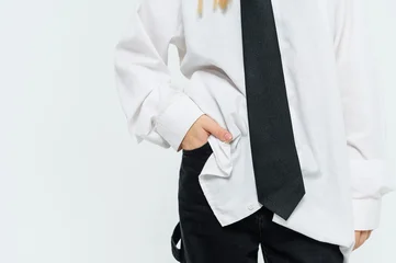 Close up of a teenage girl standing casually with one hand in a pocket while wearing an oversized white shirt and black necktie on a white studio background with copy space. © o_lypa