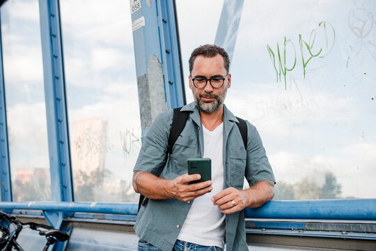 Bearded cyclist using phone while waiting for bus.