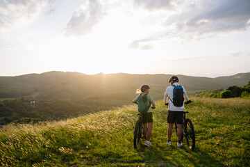 Fototapeta premium Senior couple taking break during e-bike ride, looking at sunset.