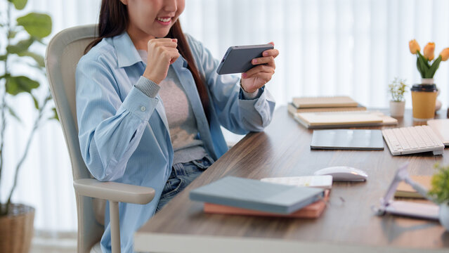 Young Asian student celebrating success while learning on tablet at home workspace with copy space