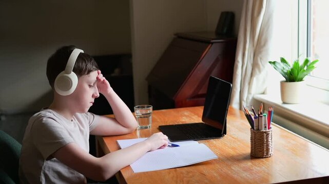 Thoughtful schoolboy tapping pen while doing homework
