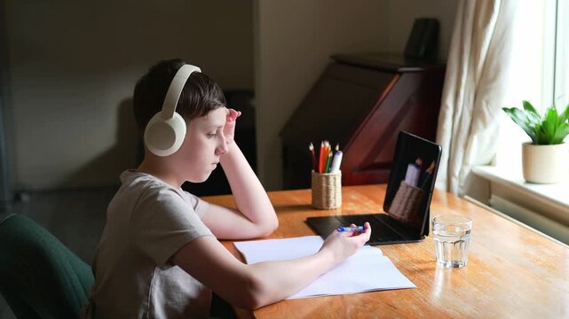 Thoughtful schoolboy twirling pen while doing homework at home