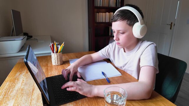 Focused schoolboy typing on laptop during home study