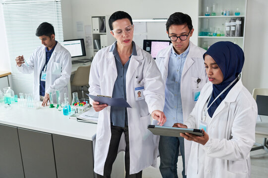 Medium shot of diverse scientists reviewing tablet and clipboard while conducting laboratory research and team training. Ideal for healthcare innovation, biotech marketing