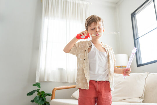 Cute little boy blowing soap bubbles in the living room, Happy young child playing with bubbles at home, Playful boy enjoying fun activity with bubble wand indoors