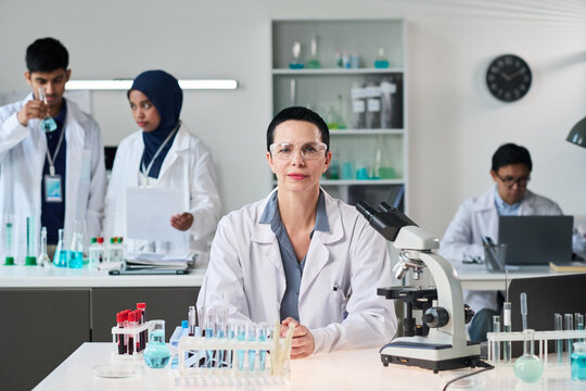 Portrait of middle aged Caucasian female scientist leading laboratory team, conducting medical research with microscope and test tubes. Ideal for healthcare innovation, biotech marketing