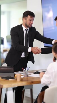 Adult male bank manager shakes hand with young couple customers during business meeting