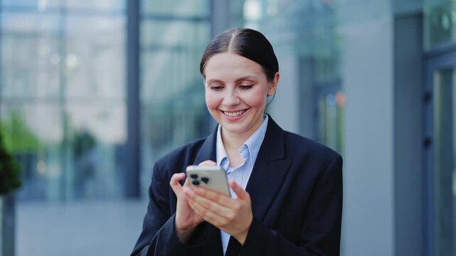 Young businesswoman, dressed in professional attire, smiles engaged with smartphone. Projects happiness and optimism, connecting in modern urban environment. Conveys joy and efficiency in daily tasks.