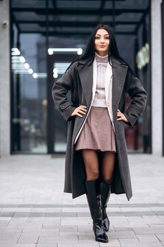 Confident woman modeling a new winter coat and boots in an urban street setting. She is looking at the camera