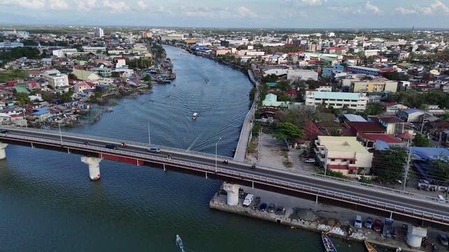 Aerial backward flight tracking a local boat navigating the waters of the Pantal River under the Jose de Venecia Bridge in Dagupan City, Philippines