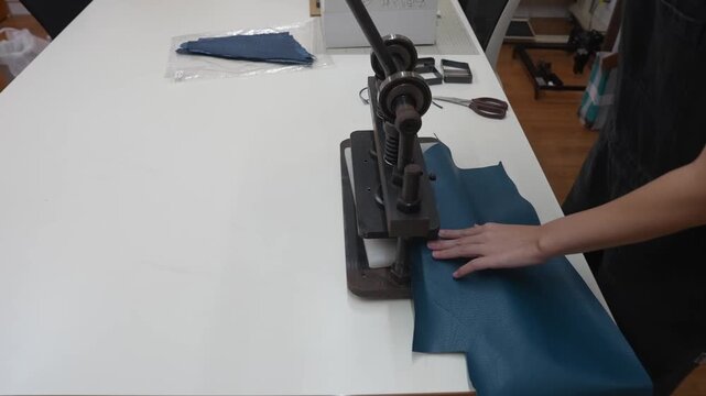 Worker pulls lever on manual arbor press to cut leather piece