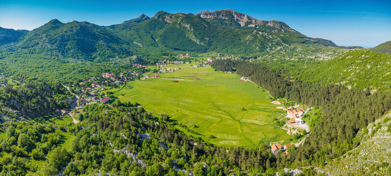Njegusi village nestled in a green mountain valley, surrounded by lush forests and towering peaks, offering a scenic panorama of Lovcen National Park