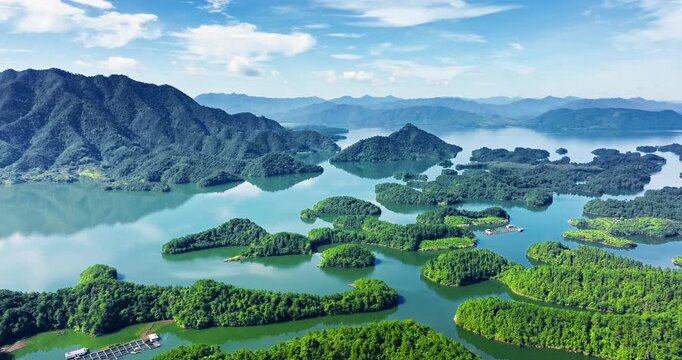 Aerial shot of Thousand Island Lake showing green forested islands scattered across the turquoise water under a blue sky in Zhejiang, China.
