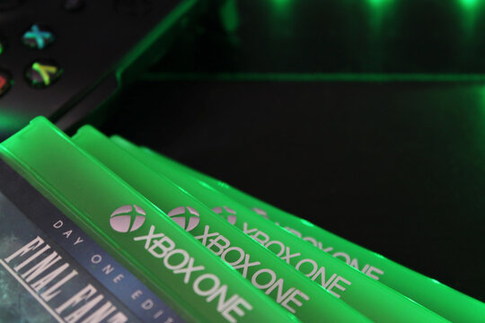 Xbox One game cases and controller with green ambient lighting. Close up disc details. Modern gaming collection showcasing console entertainment, video game culture, technology, and home setup.