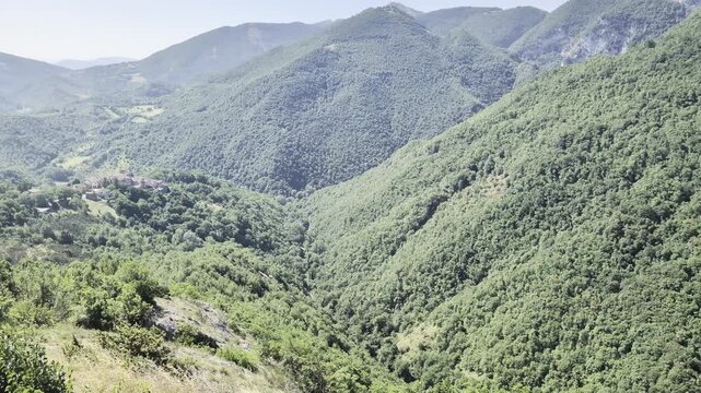 Ampio panorama montano con pendii verdi ricoperti di vegetazione fitta e vallate profonde che si estendono verso l&rsquo;orizzonte sotto un cielo limpido