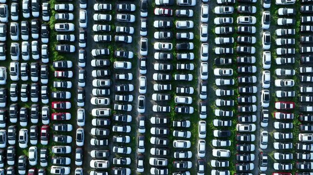 Drone perspective of rows of internal combustion and electric vehicles in storage, illustrating the transition between conventional mobility, EV adoption, and shifting global automotive markets. 4k.
