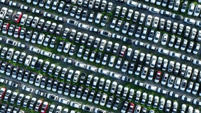 Overhead drone shot of large automobile inventory storage, symbolizing economic recession, supply chain imbalance, overproduction, and rising warehouse costs across the automotive industry. 4k.
