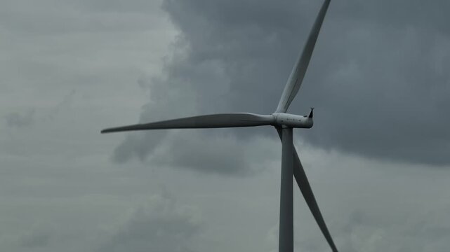 Drone perspective of a wind turbine surrounded by dramatic gray clouds, reflecting sustainable power generation, climate uncertainty, energy security, and engineering built to endure harsh conditions.