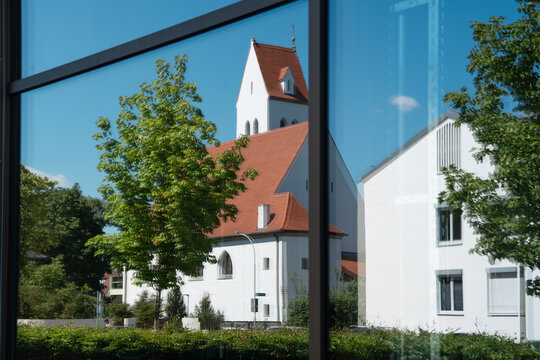 Reflection of Evangelical Lutheran Erloeserkirche church in large modern glass window in Fuerstenfeldbruck, Bavaria, mix of historic Protestant architecture and contemporary building facade in Germany