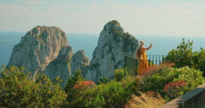 Woman taking photo of Faraglioni sea stacks from garden viewpoint in Capri