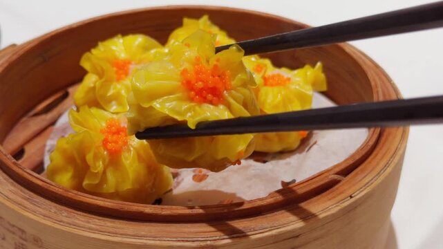 Cantonese Yellow Shumai Dim Sum Lifted by Chopsticks in Bamboo Steamer