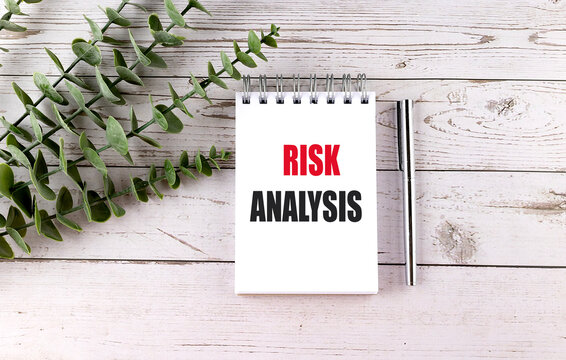 Risk analysis concept on notepad with pen and green leaves on wooden background representing business assessment