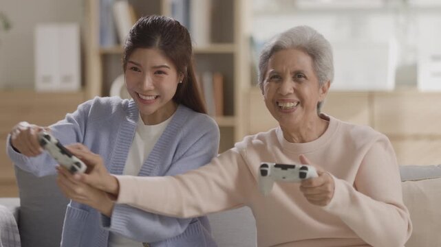 Young woman and senior grandmother play video game with controller in living room showing excited competitive emotions enjoying happy leisure time bonding together as family across generations