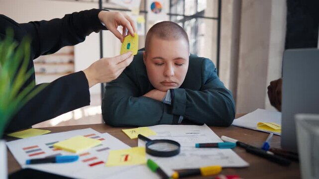 Coworkers sticking notes with fake eyes on face of sleeping woman in meeting. Boring business meeting in office, tired and exhausted office worker, overwork and extra hours felt asleep at workplace