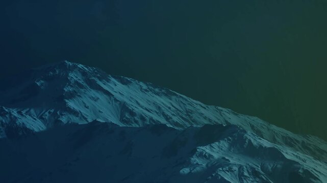 A snow covered mountain is seen at night with a dark sky overhead. The mountain shows a mix of blue and green hues. The scene captures natures vastness and beauty.