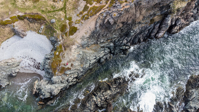 Aerial view of person in red jacket explores rugged coast