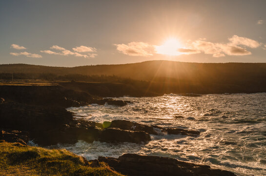 Golden sun setting over a rocky ocean shoreline in Newfoundland