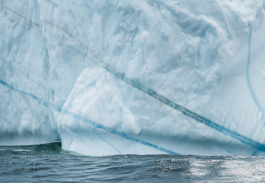 Close up of massive iceberg wall with blue stripes at sea
