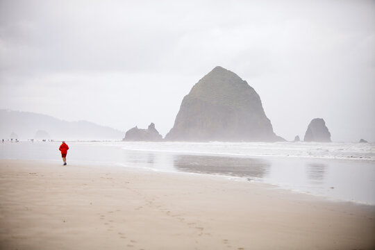 Lone person in red jacket walks on misty beach